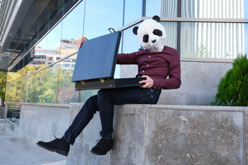 Male robber wearing a panda head mask have stolen a briefcase and is opening it. Bizarre thief. © Ladanifer