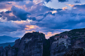 Twilight over Varlaam and Great Meteoron monasteries in Meteora, Greece. Underexposed, great sunset with clouds and sun rays. UNESCO World Heritage