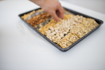 Male hand picking nuts from a black tray with seeds and nuts