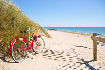 Fototapeta premium Vieux vélo rouge en bord de mer le long d'une plage en France.