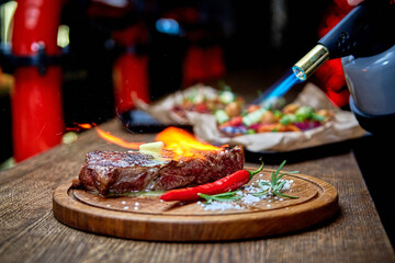 Master chef cooking barbecue Beef Grilled steak meat with fire flames on wooden table