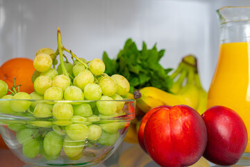 Glass pitcher of orange juice and fruits on fridge shelf