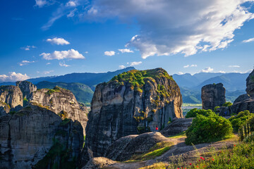 Fototapeta na wymiar Evening in typical Meteora landscape, Greece. Massive rocks, cliffs, mountains and valley. Few tourist enjoy the view. Blue sky and great clouds.
