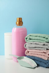 Detergent, scoop with powder and towels on white table against blue background