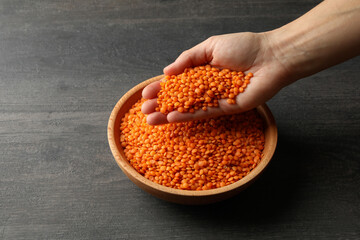 Female hand holds red legumes over a bowl of legumes on dark background