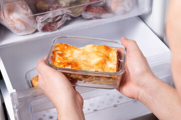 A person is taking a container of frozen casserole or lasagne out of the freezer. Concept of ready...