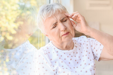 Stressed senior woman suffering from headache at home