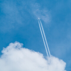 Plane flying with white trail over white cloud in blue sky