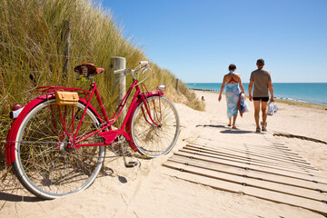Balade en bord de mer, deux touristes dans les dune, un vieux vélo rouge sur le bord du chemin.