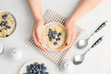 Female hands with tasty oatmeal and blueberry in bowls on table