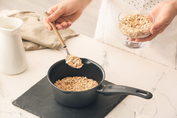 Woman cooking tasty oatmeal on table in kitchen