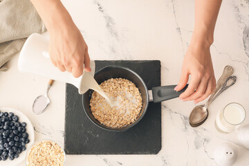 Woman cooking tasty oatmeal with blueberry on table in kitchen