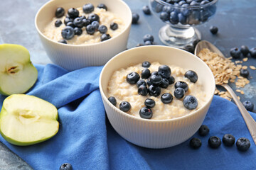 Bowls with tasty oatmeal and blueberry on color table