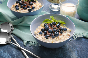 Bowls with tasty oatmeal and blueberry on color table