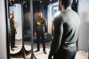Stylish casual african american man at fitting room clothes store, looking on mirror. The concept of stylish men's clothing.