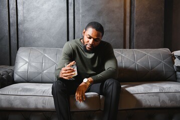 Handsome young african american man in elegant suit with glass of whiskey relaxing on sofa