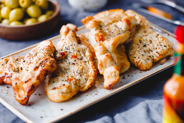 Grilled turkey escalopes with hot sauce on a table.