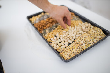 Male hand picking nuts from a black tray with seeds and nuts