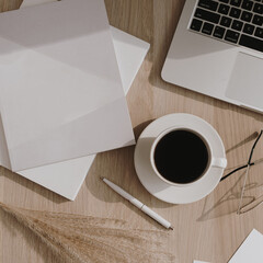 Flatlay of coffee cup, laptop, pampas grass, notebook on wooden table. Flat lay, top view morning breakfast and work concept.