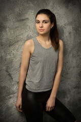 Fototapeta premium beautiful sexy girl in a gray tank top and black pants posing against the background of an old cracked wall