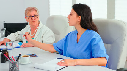 Fototapeta premium Close up of medical nurse taking notes on clipboard during healtchare meeting with coworkers in hospital boardroom. Clinic expert therapist talking with colleagues about disease, medicine professional
