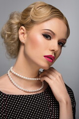 portrait of a beautiful blonde girl in a black dress with white polka dots and a necklace of pearls posing in the studio on a gray background