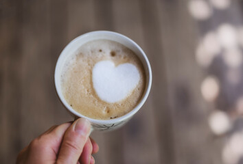 A cup of coffee with a heart in a white cup in a hand.
