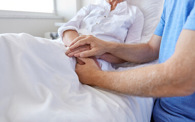 Obraz premium medicine, healthcare and people concept - senior man visiting and cheering his woman lying in bed at hospital ward