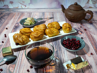 Tea drinking with delicious sweets. On the table are a cup of tea, a kettle, profiteroles, sweets and lingonberries. Near the cup there is a piece of candy partially unpacked. Background with dessert.