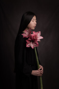 Classic painterly studio portrait of young woman in black dress with a giant pink amaryllis flower