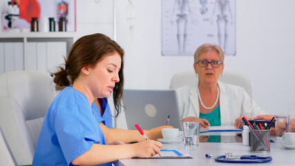 Nurse checking list of patients during brainstorming, discussing with colleagues and taking notes...