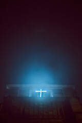 leuchtendes Kreuz am Kirchturm nachts im Nebel