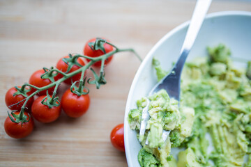 Cherry tomatoes and bowl of mashed avocado on wooden table