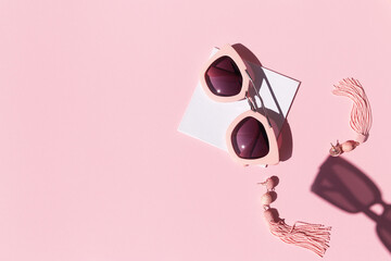 Composition made with woman accessories. Sunglasses and earrings on pink background.