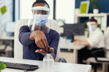 Fototapeta na wymiar Close up of african woman using hand sanitizer during global pandemic with coronavirus. Businesswoman in new normal workplace disinfecting while colleagues working in background.