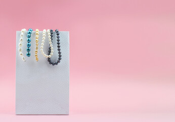 Mixed colors pearl beads hanging on a white package on pink background, copy space, mock-up.