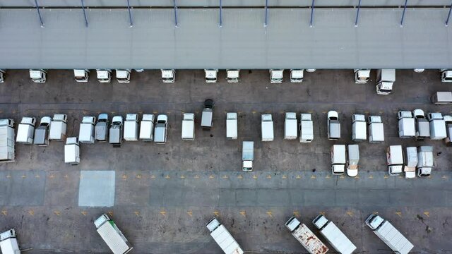 Aerial view logistics center in industrial city, Industrial warehouse loading dock where many truck with semi trailers load merchandise, Trucks loading at logistic center goods warehouse.