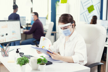 Business consultant on a call with consultant using wireless headphones during covid-19. Employees with visors working in corporate company workspace respecting social distance analysing data and