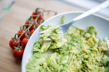 Cherry tomatoes and bowl of mashed avocado on wooden table