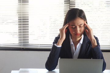 Asian businesswoman sitting and using her hands touching her head feeling sick and got headache due...