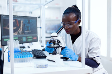 African researcher adjusting microscope lenses looking at sample on glass slide. Black healthcare...