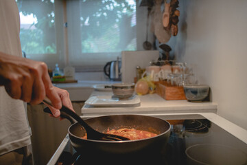 Closeup of man cooking pasta sauce in the kitchen with black pan.