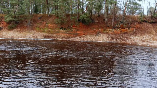 Red sandstone cliffs in the banks of river Salaca during late autumn time, Latvia. Real time drone footage
