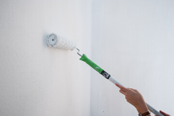 Renovierung einer Wohnung - Eine Farbrolle an einer weißen Wand mit Raufaser Tapete