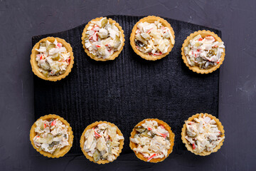 Salad tartlets with pineapple and shrimps on a black wooden board on a gray concrete background.