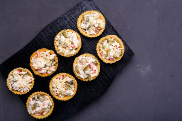 Tartlets with pineapple and shrimp salad on a black wooden board on a gray concrete background copy space