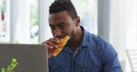 African american businessman using laptop and eating croissant in cafe