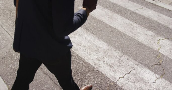 Low section of african american businessman carrying takeaway coffee walking on zebra crossing