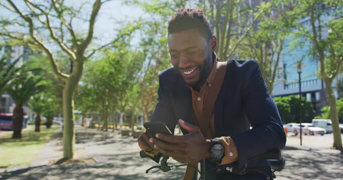 Smiling african american businessman using smartphone leaning on bike