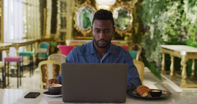 African american businessman using laptop drinking coffee in cafe